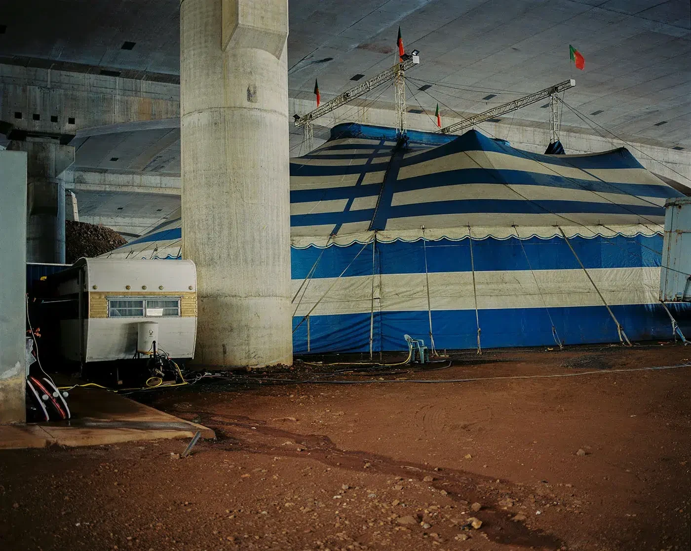 A blue-and-white striped tent stands beneath concrete viaduct columns.