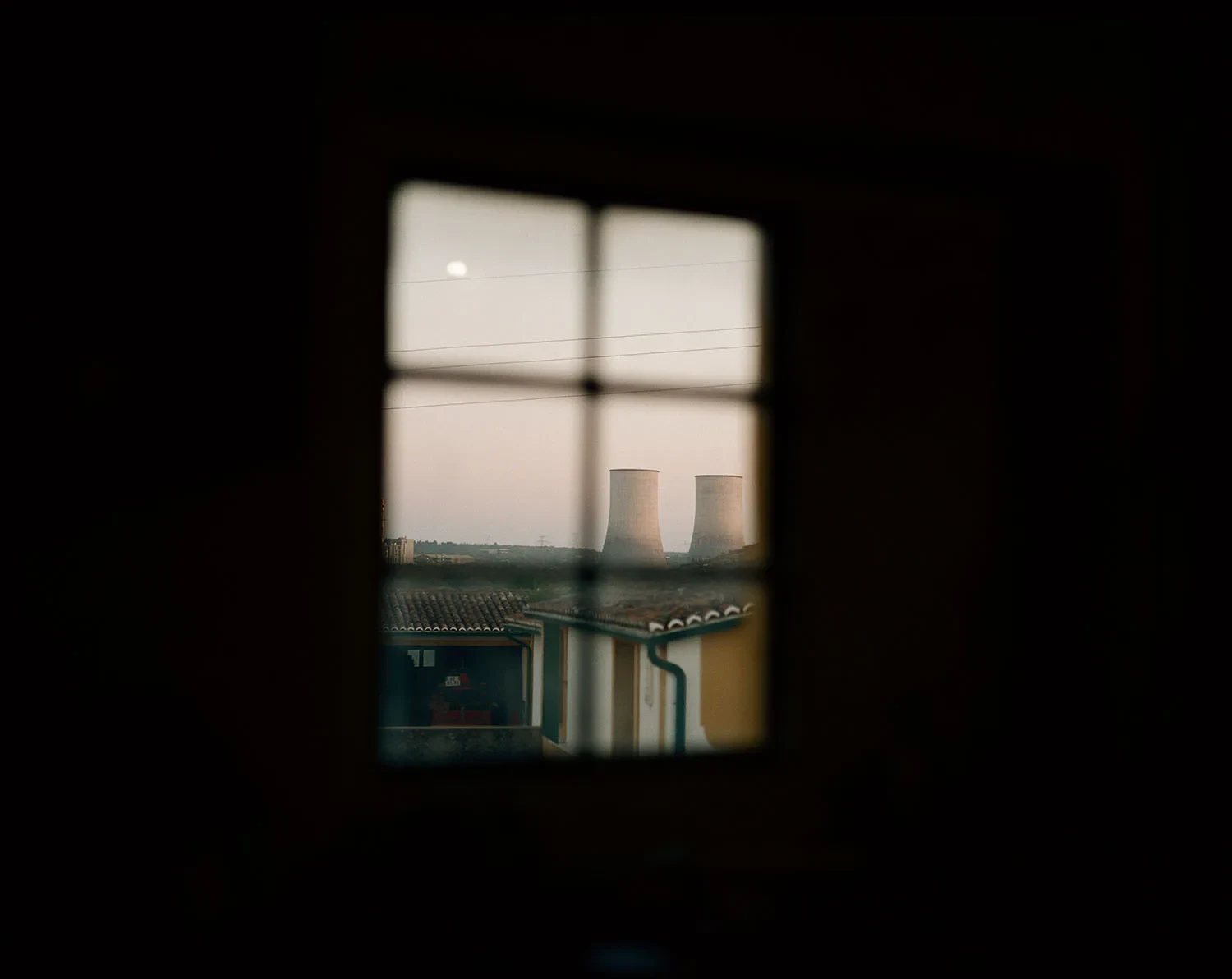 A blurred window in a dark interior frames buildings and a distant concrete structure.