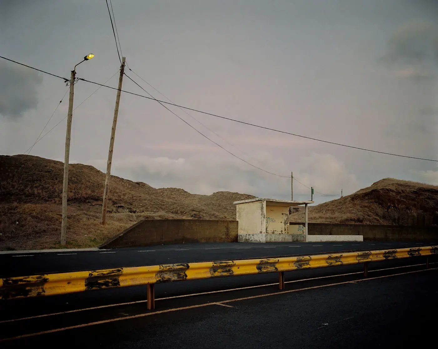 A roadside building and utility poles stand against bare hills beneath a grey sky.