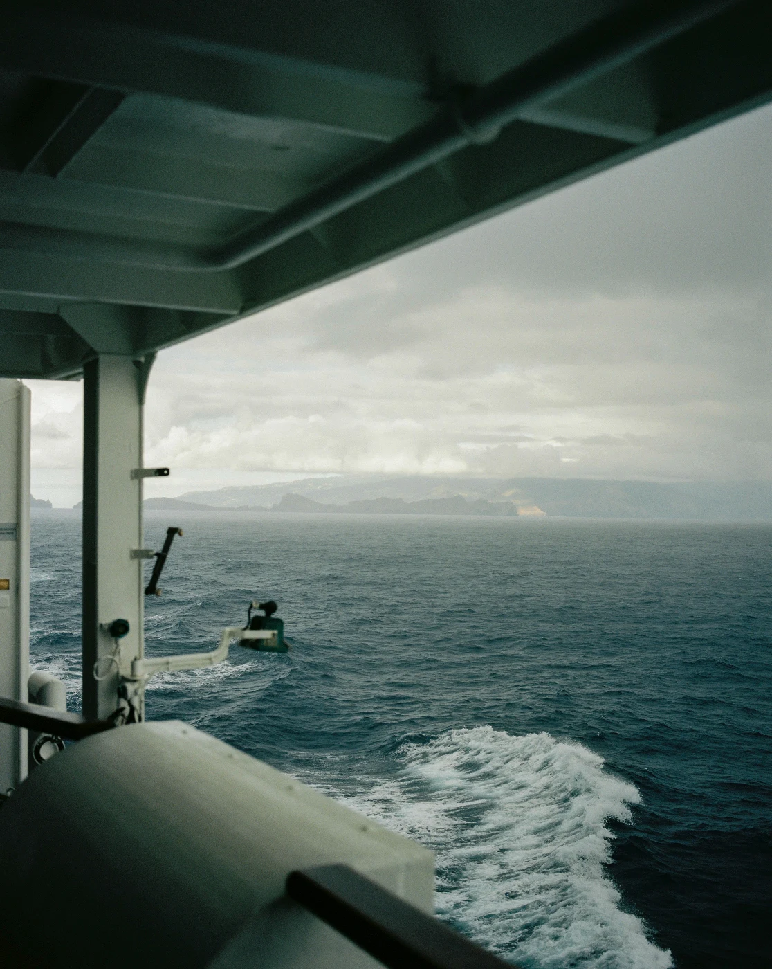 The sea and distant coast seen beneath the roof of a vessel, with white wake below.