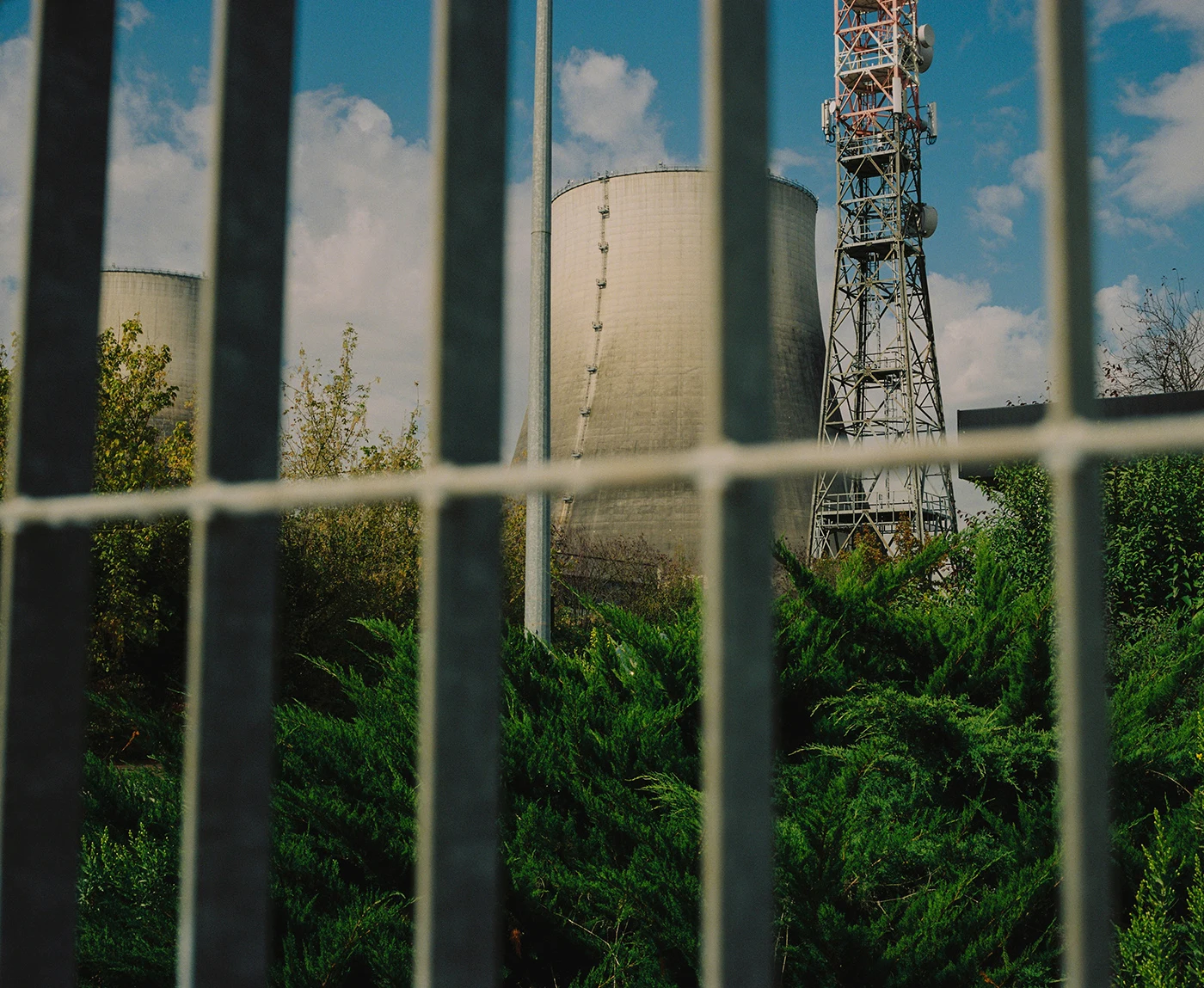 Metal fence bars frame a cylindrical tank, vegetation and a communications mast.