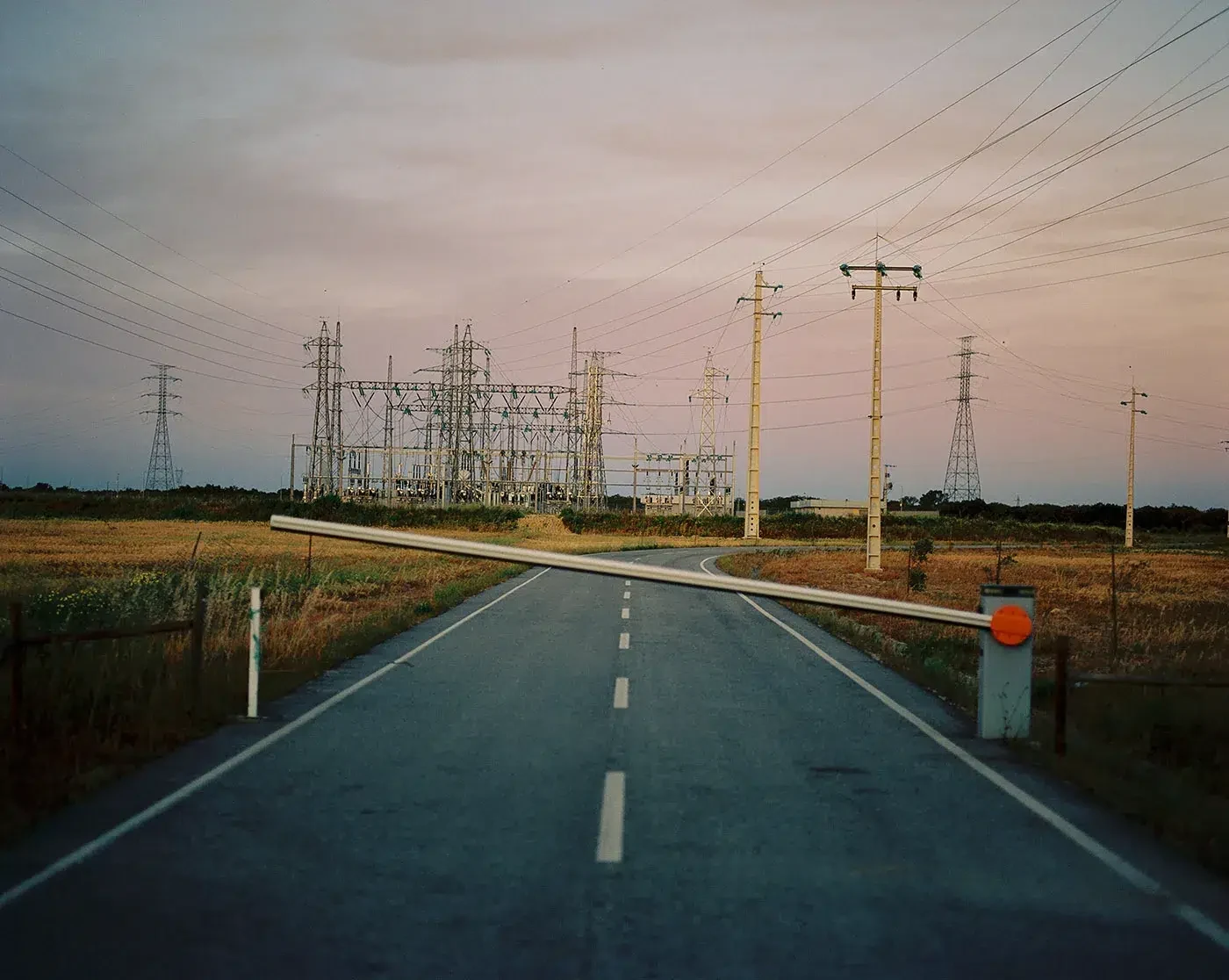 Uma barreira fecha uma estrada que conduz a uma subestação elétrica e a linhas de alta tensão.