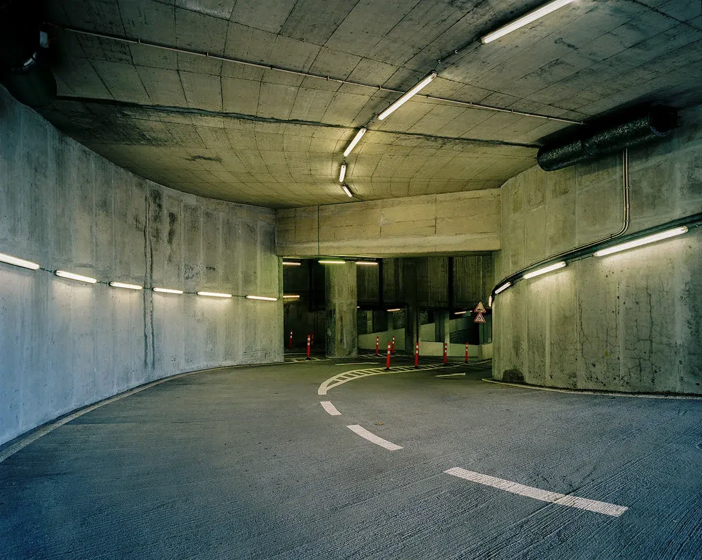 Uma estrada curva no interior de um túnel de betão iluminado por lâmpadas fluorescentes.