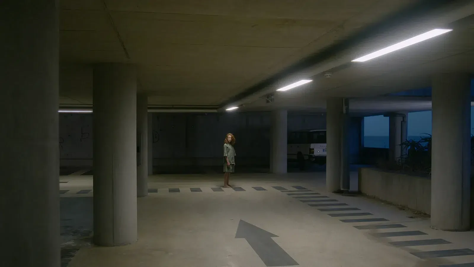 Duas figuras à distância entre colunas de betão de um parque de estacionamento.