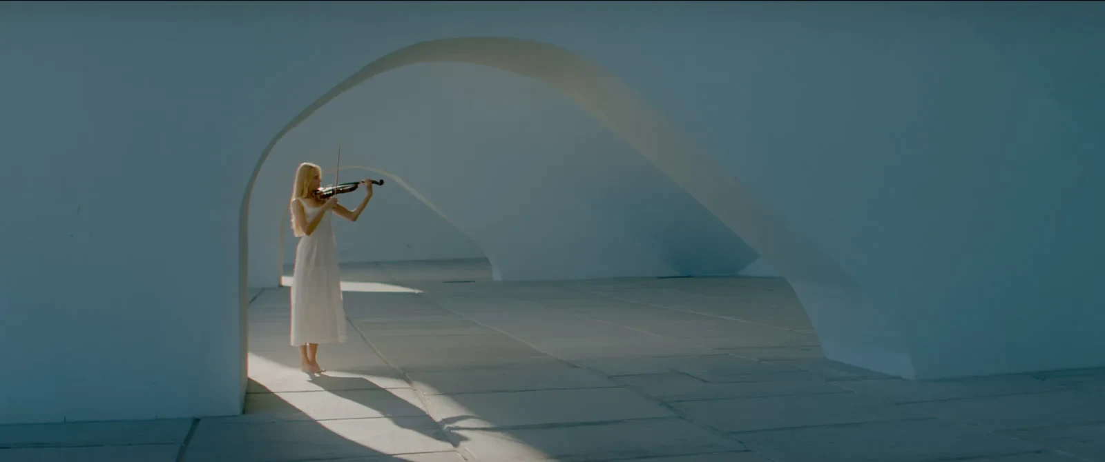 Uma pessoa a tocar violino junto a um arco branco iluminado pelo sol.