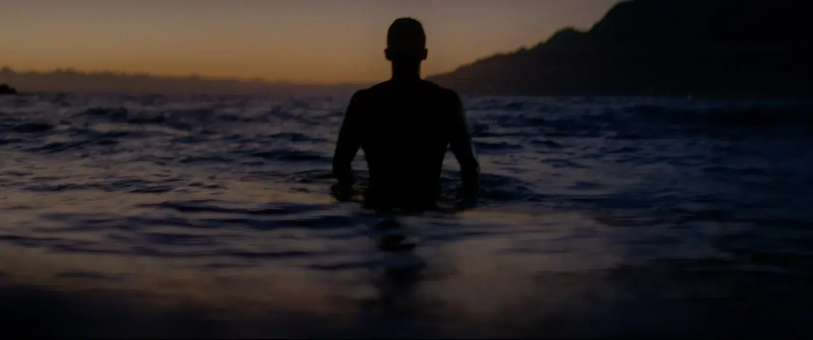 A silhueta de uma pessoa dentro do mar ao anoitecer.