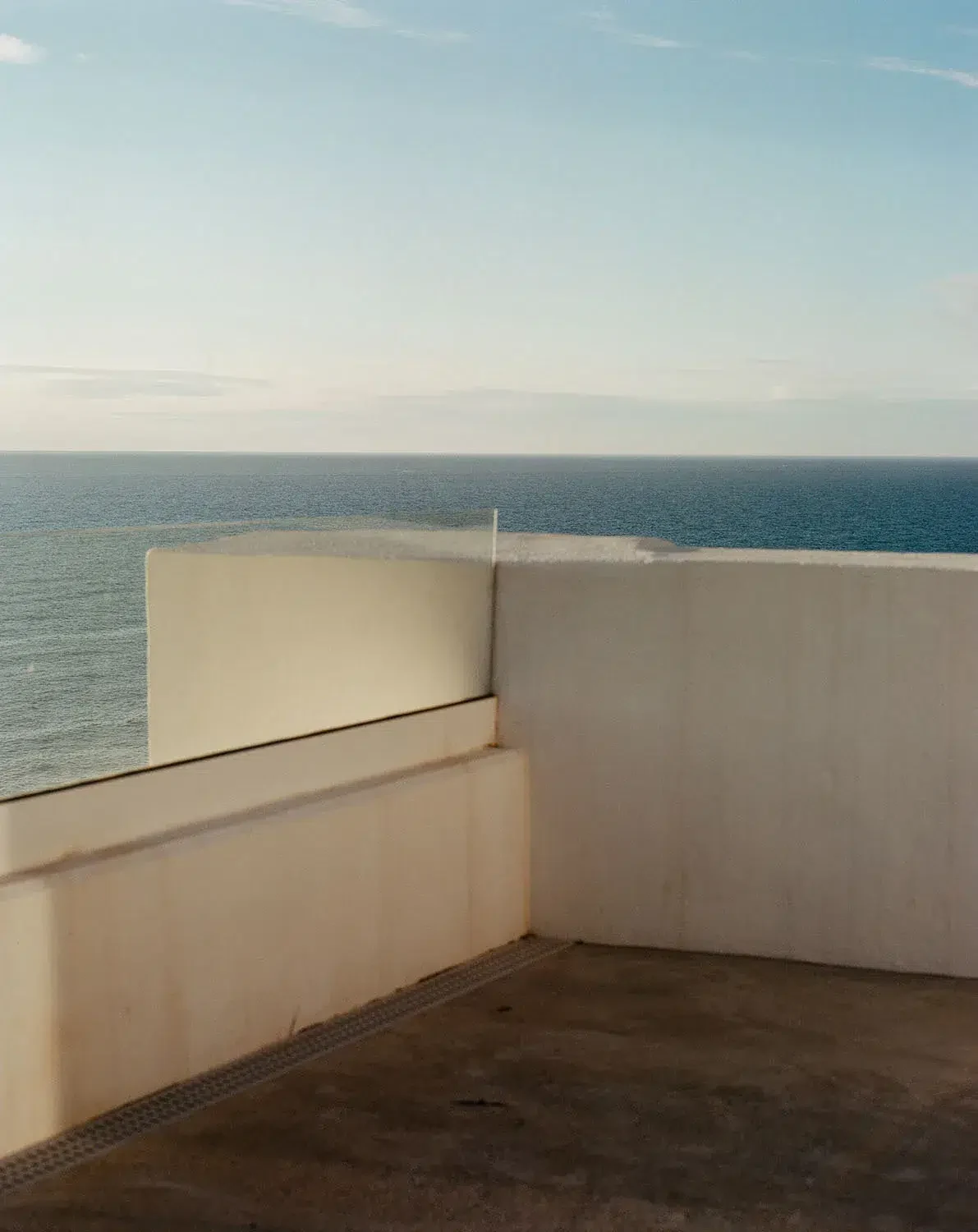 O canto de um terraço de paredes claras dá para o mar sob um céu azul.