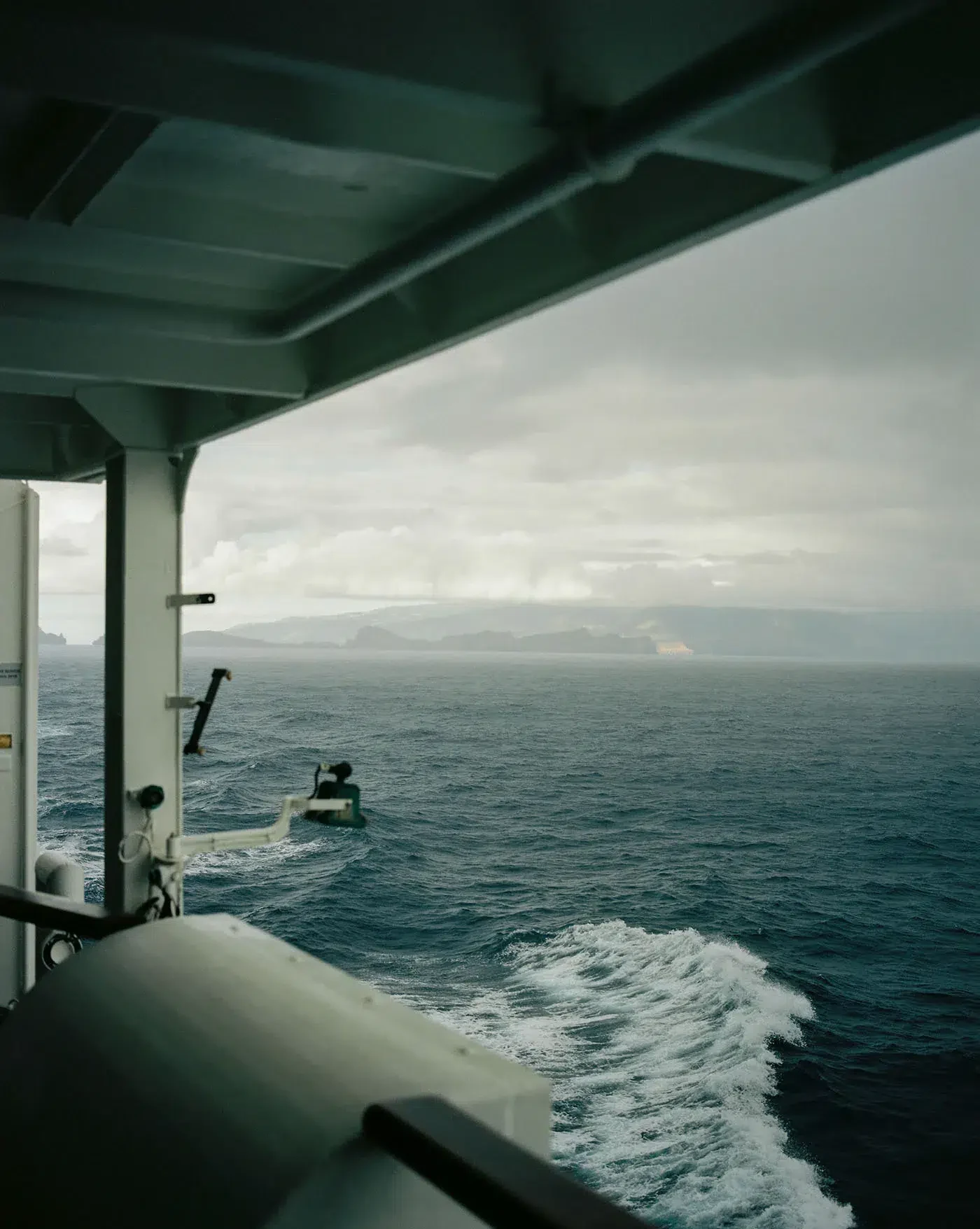 The sea and distant coast seen beneath the roof of a vessel, with white wake below.