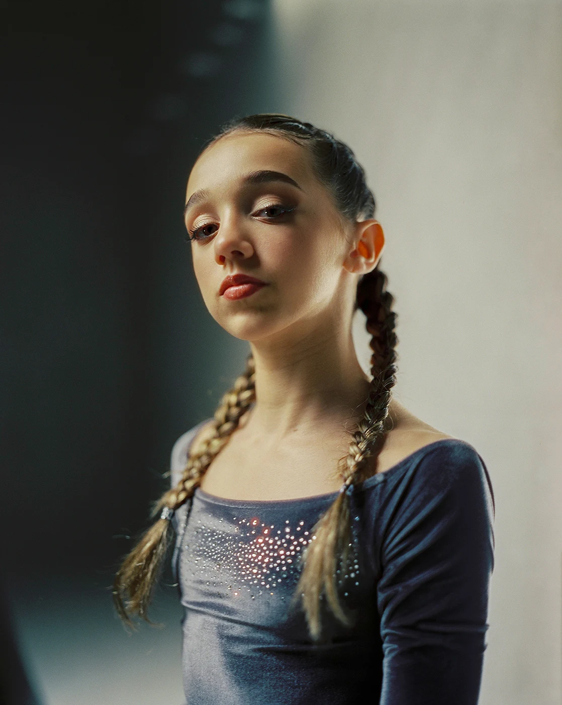 Portrait of a person with braided hair, lit from one side against a dark background.