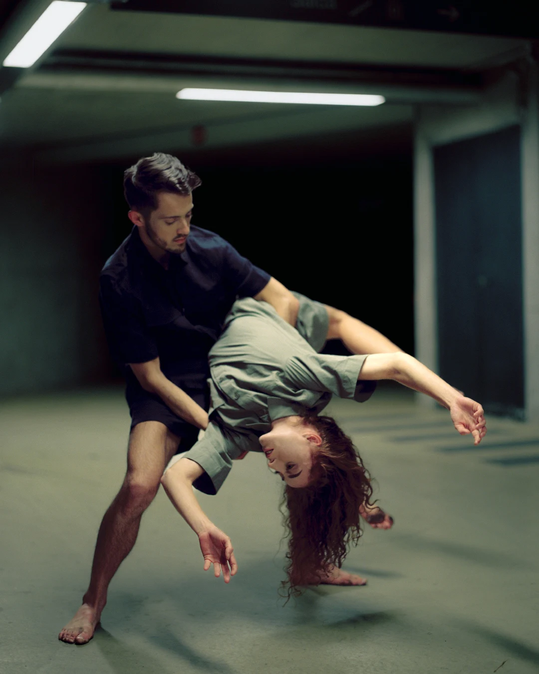 Uma pessoa apoia outra numa inclinação lateral profunda, próxima do chão, numa pose de dança.
