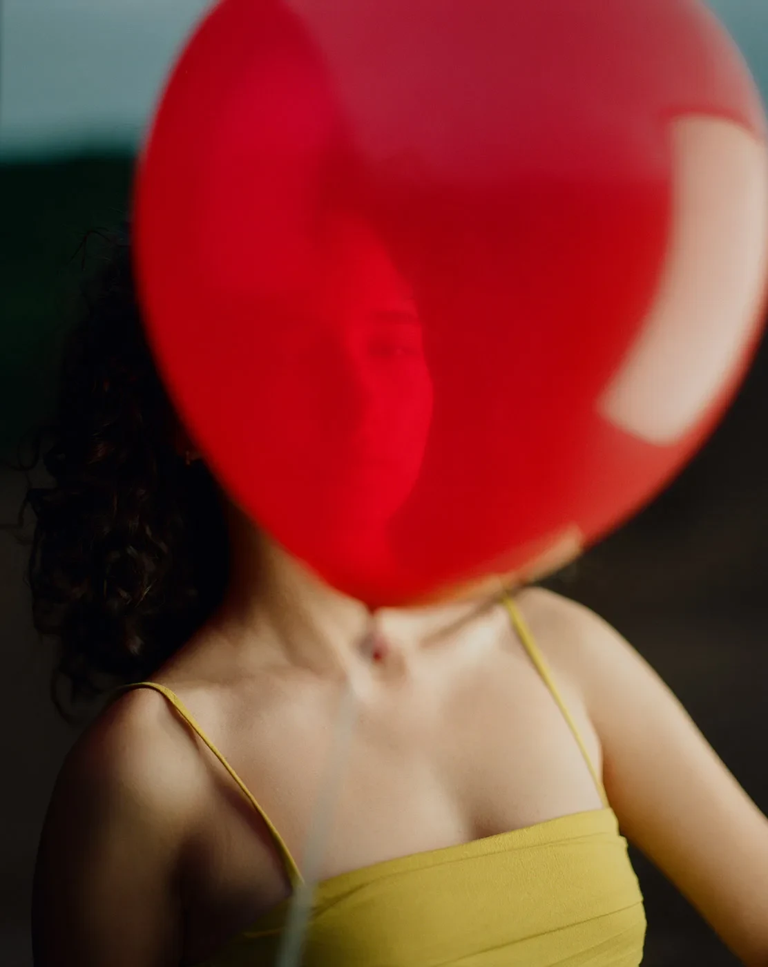 Um balão vermelho oculta o rosto de uma pessoa com uma camisola amarela.