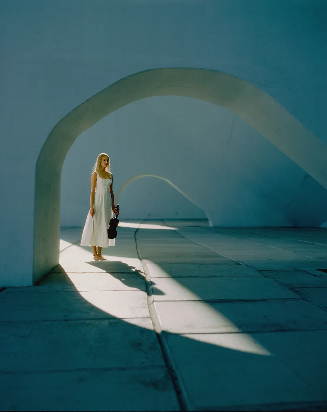Uma pessoa com um vestido claro está ao sol sob arcos azuis curvos.