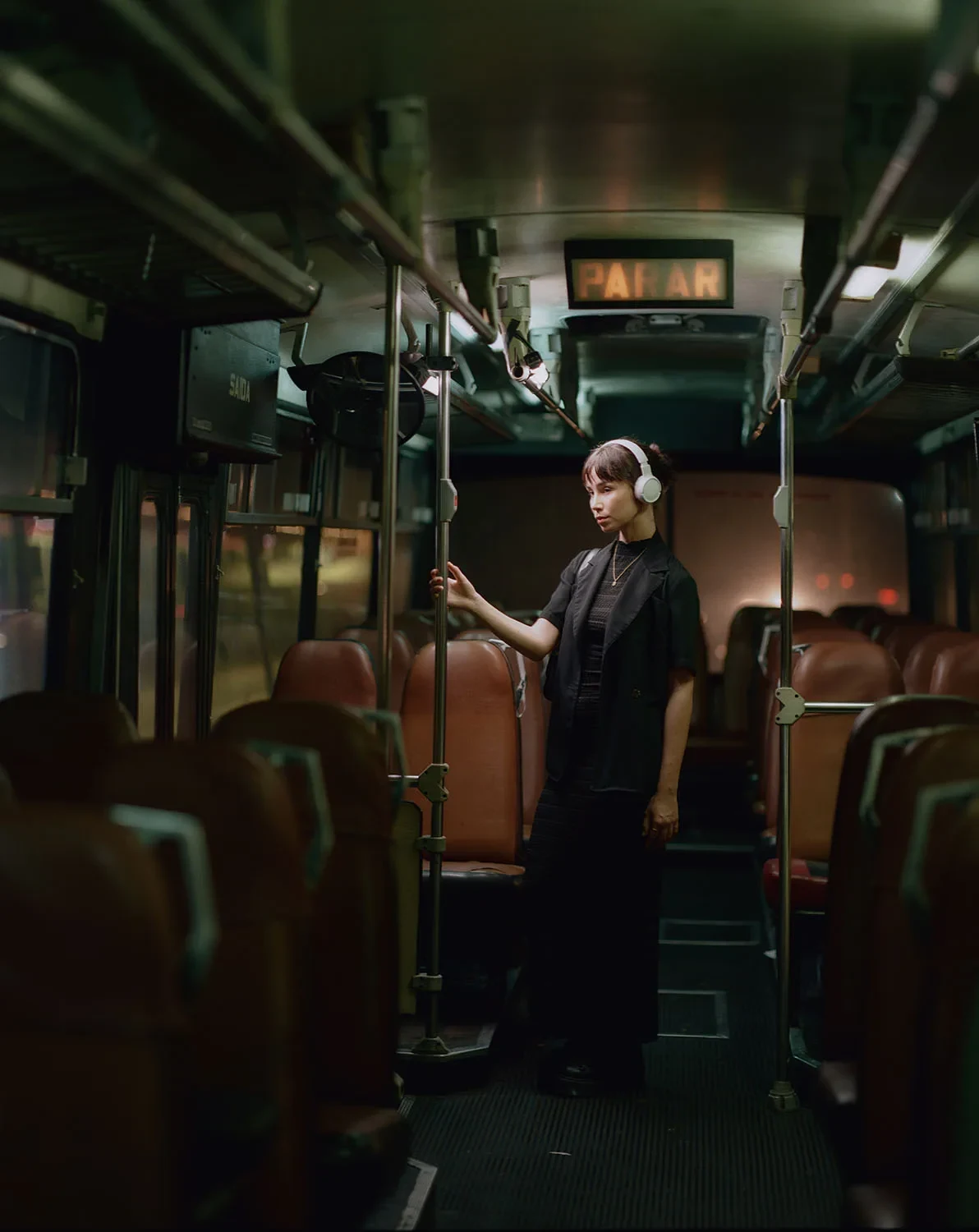 A person wearing headphones stands in the aisle of a bus with brown seats.
