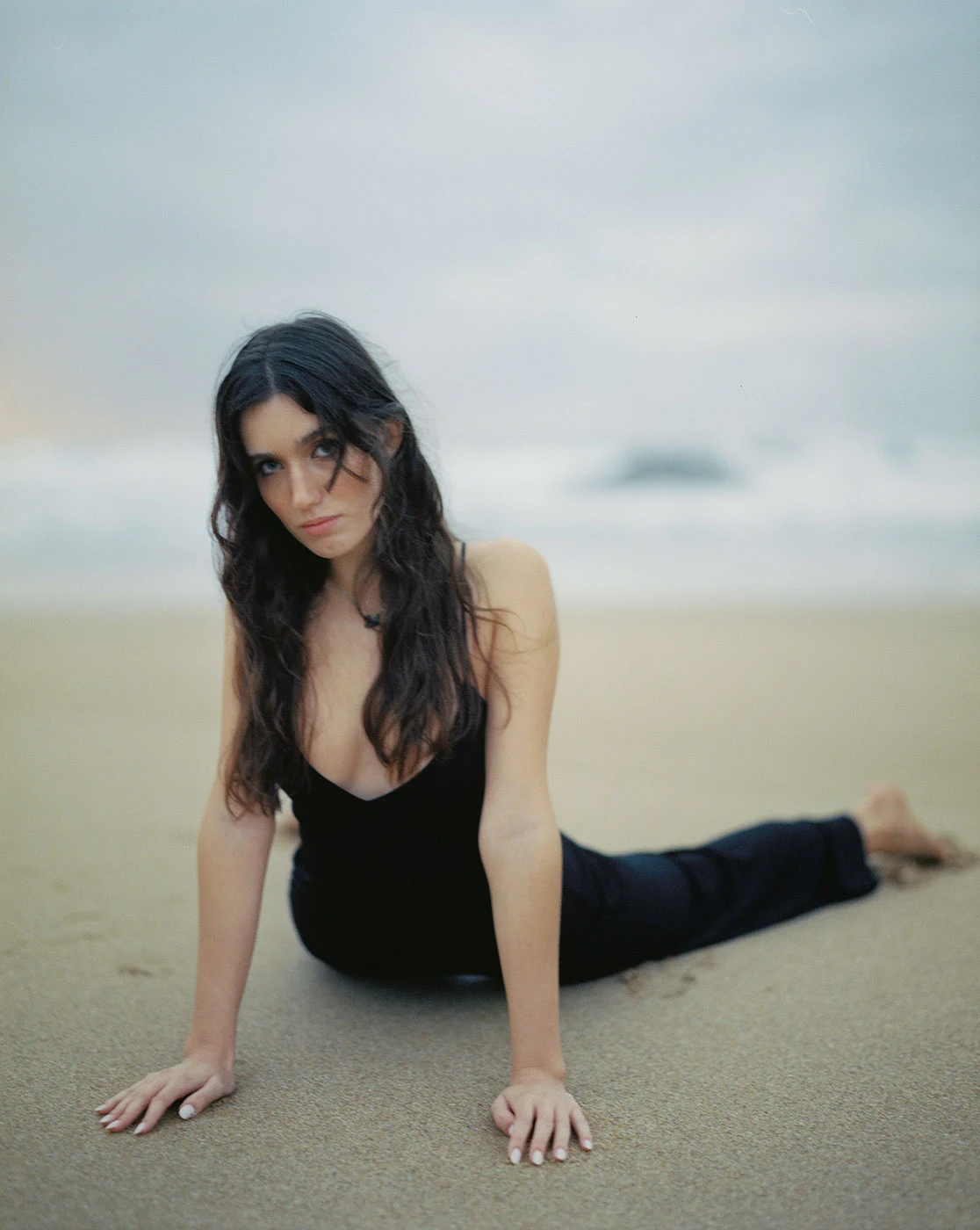 Uma pessoa vestida de preto alonga-se na areia junto ao mar.