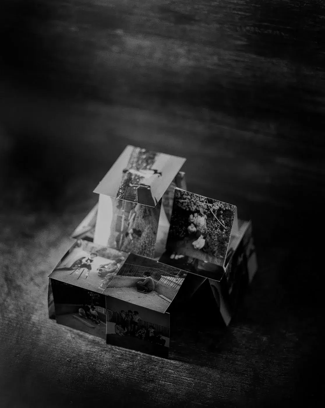 Fotografia a preto e branco de fotografias impressas dispostas sobre caixas numa superfície escura.